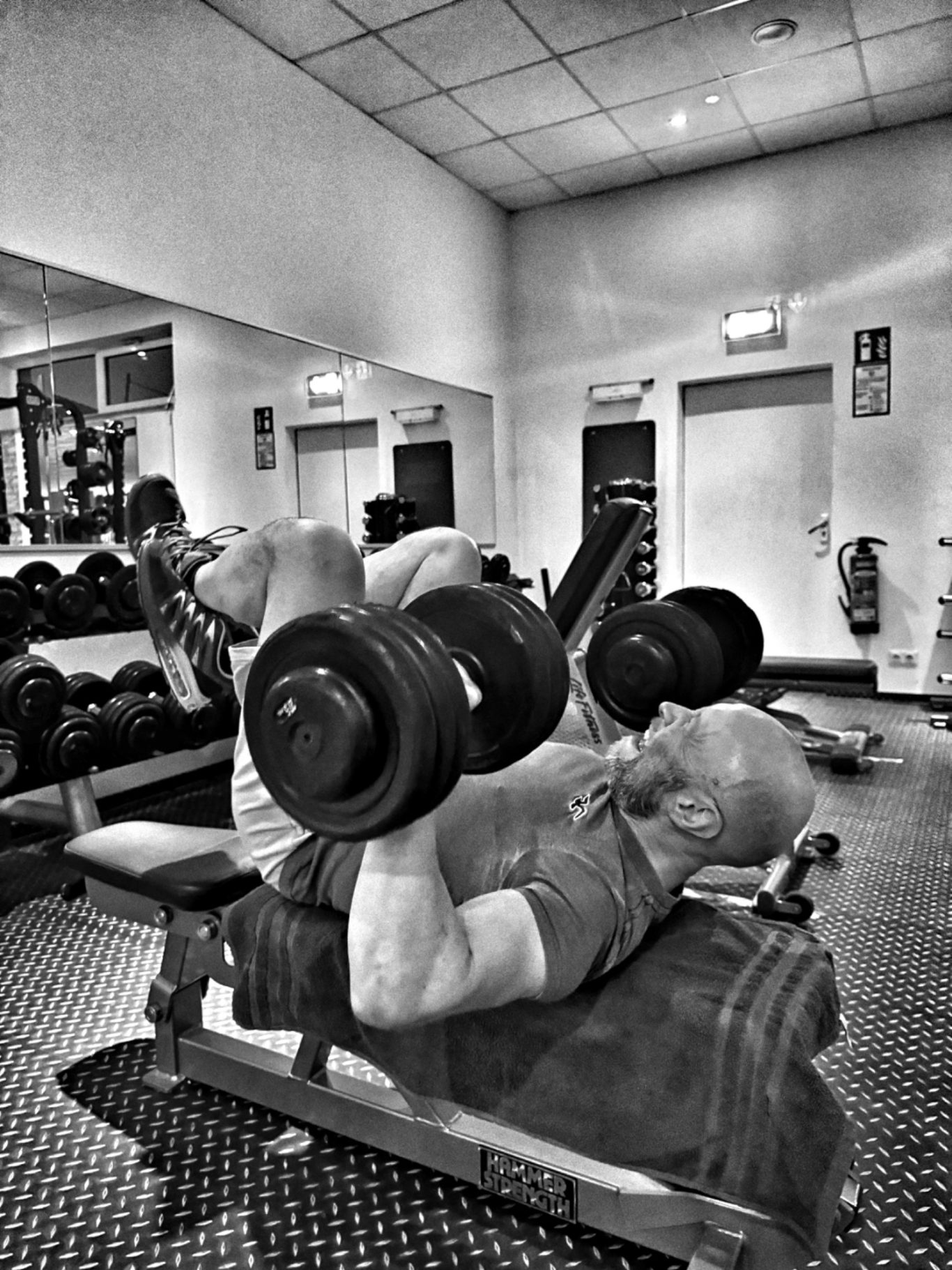 Mann trainiert im Fitnessstudio mit Hanteln auf einer Bank.
