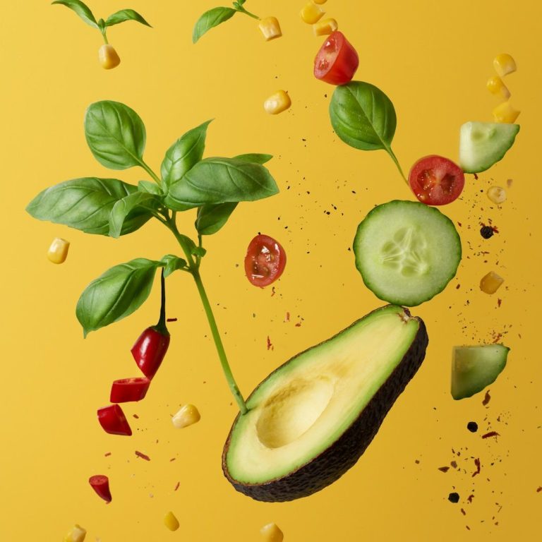 Avocado, Gurkenscheiben, Tomaten, Basilikum vor gelbem Hintergrund