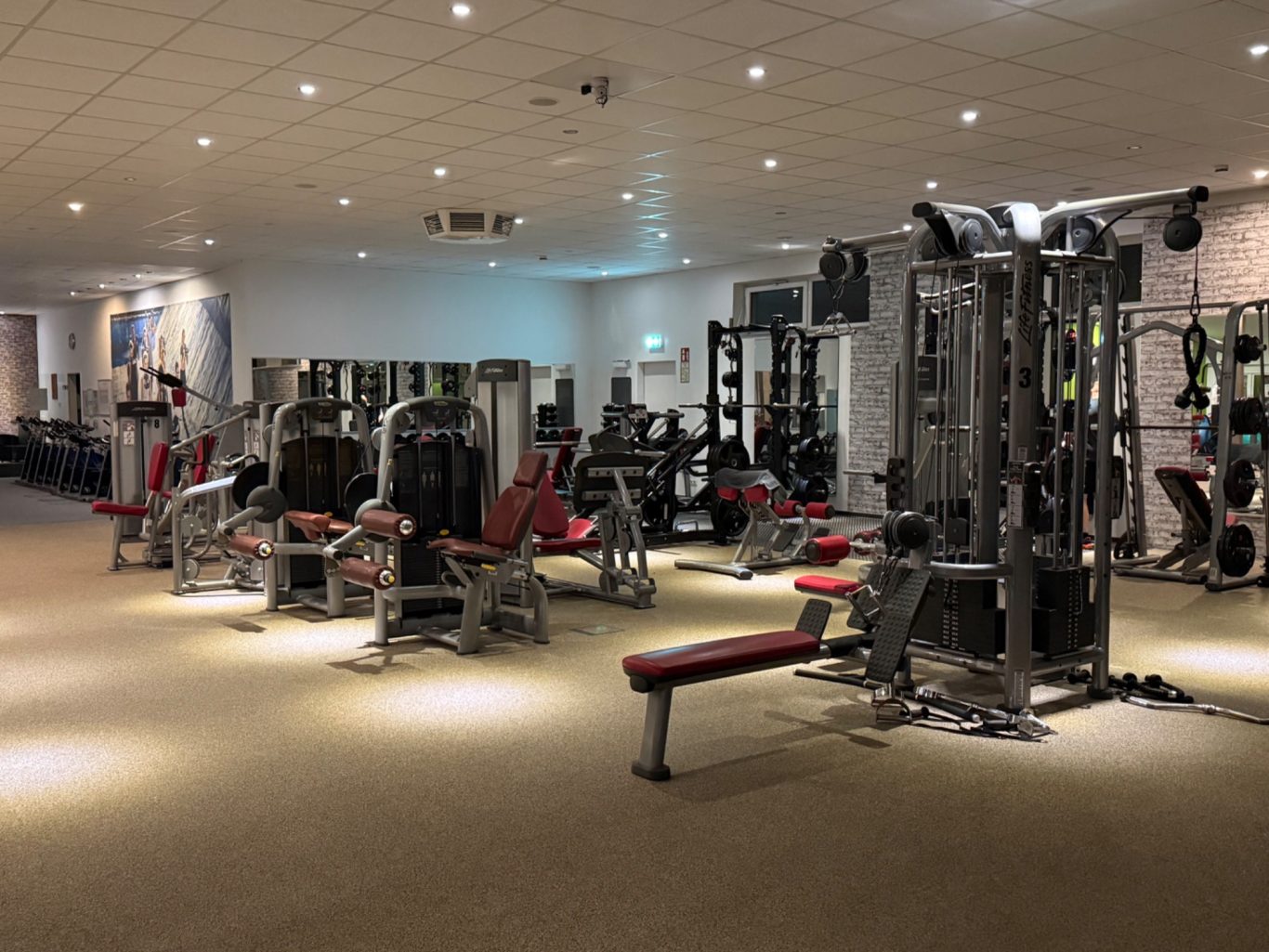 Fitnessstudio mit verschiedenen Trainingsgeräten und Kursräumen. Gut beleuchtet und modern.
