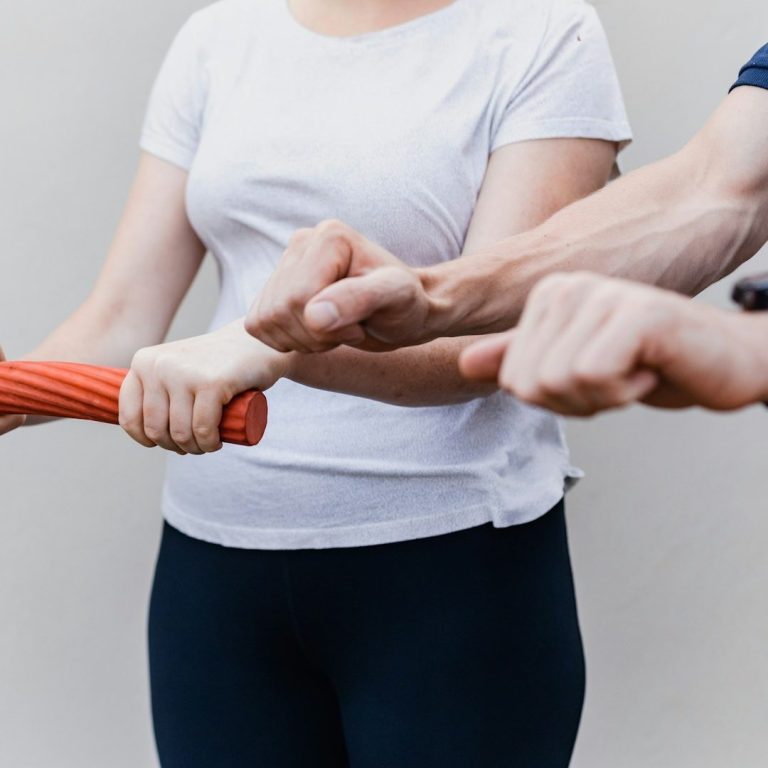 Oberkörper einer Frau beim Training mit einem Stab als Hilfsmittel
